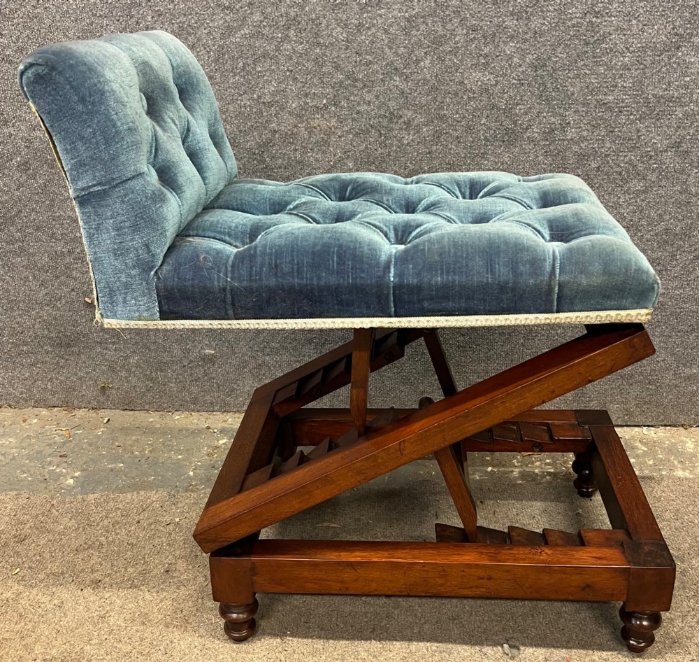 A 19th-century mahogany gout stool featuring an adjustable ratcheted frame and button-tufted blue velvet upholstery on turned feet.