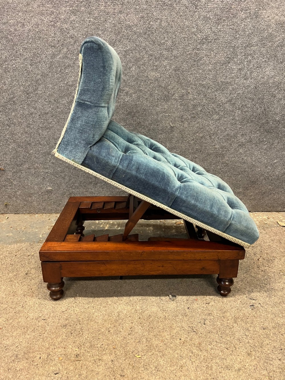 A 19th-century mahogany gout stool featuring an adjustable ratcheted frame and button-tufted blue velvet upholstery on turned feet. View II