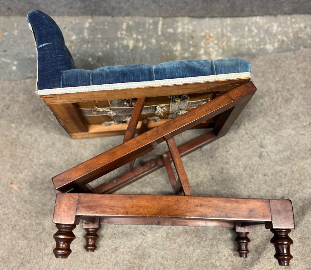 A 19th-century mahogany gout stool featuring an adjustable ratcheted frame and button-tufted blue velvet upholstery on turned feet. View VI