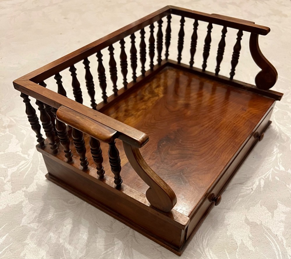 An antique yew wood desktop book trough featuring turned spindle gallery railings on three sides and a smooth timber base.