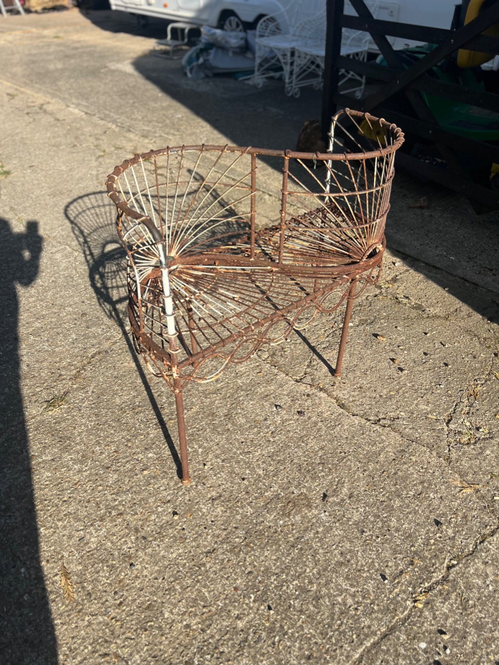 A weathered brown wrought iron S-shaped conversation seat featuring fan-patterned wire backrests and a looped apron base. View II