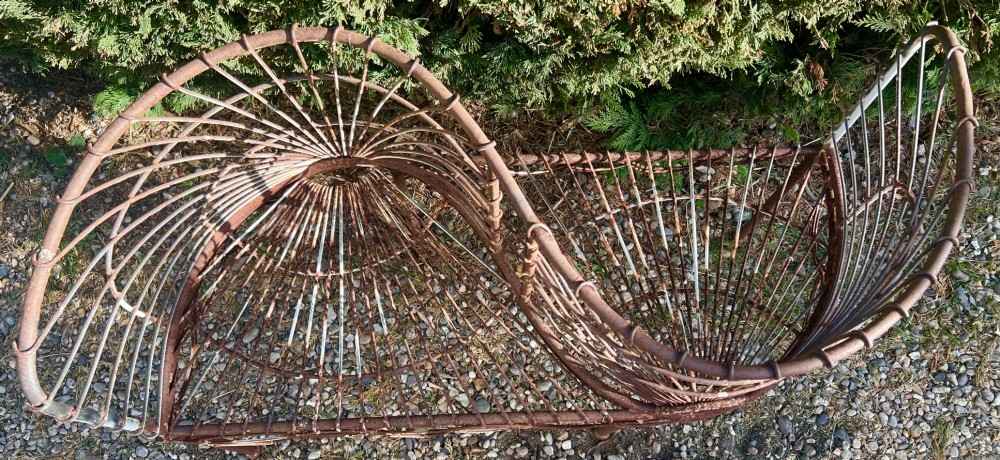 A weathered brown wrought iron S-shaped conversation seat featuring fan-patterned wire backrests and a looped apron base. View V