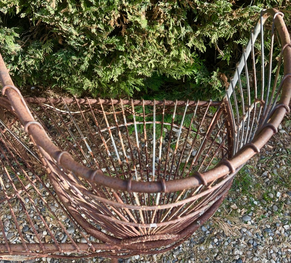 A weathered brown wrought iron S-shaped conversation seat featuring fan-patterned wire backrests and a looped apron base. View VI