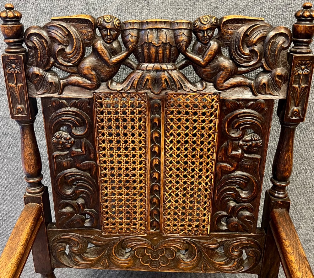 A dark carved oak Carolean style armchair featuring high cane back panels, a cane seat, scrolled armrests, and cherub crestings. View III