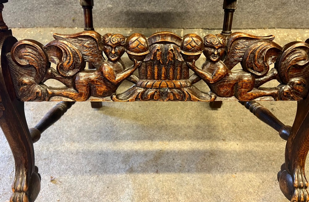 A dark carved oak Carolean style armchair featuring high cane back panels, a cane seat, scrolled armrests, and cherub crestings. View VI