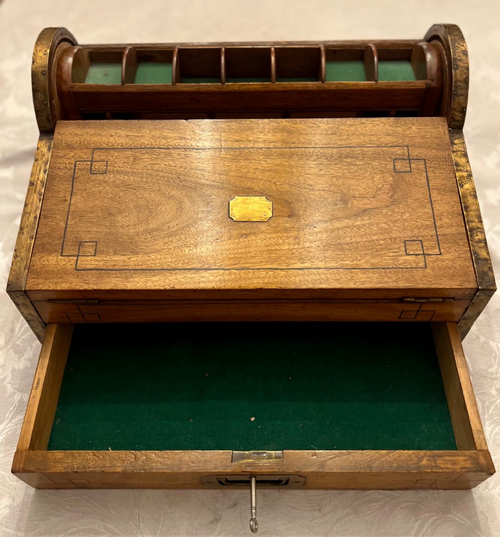 An Anglo Indian camphorwood campaign writing box featuring a ribbed tambour top section, protective brass corner strapping, geometric inlay, and a central brass plaque. View II