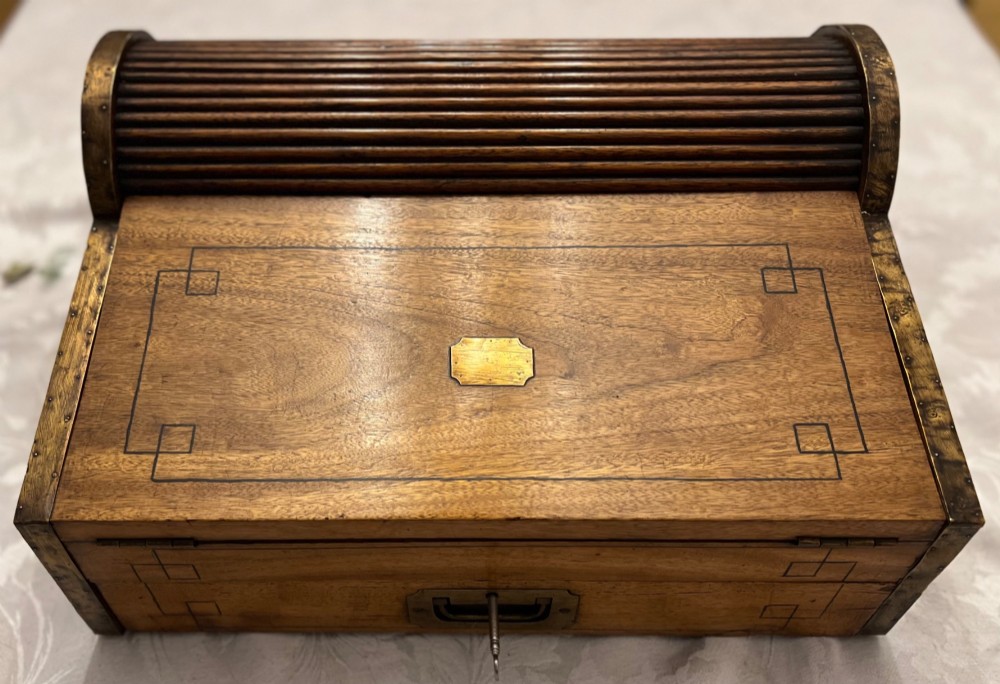 An Anglo Indian camphorwood campaign writing box featuring a ribbed tambour top section, protective brass corner strapping, geometric inlay, and a central brass plaque. View VII