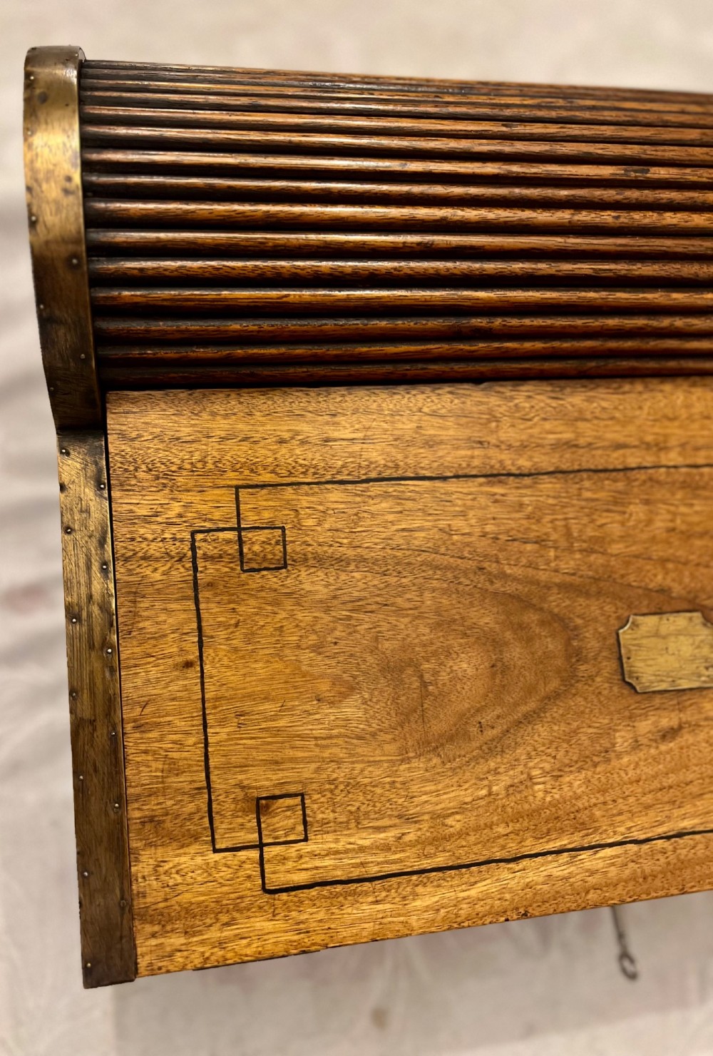 An Anglo Indian camphorwood campaign writing box featuring a ribbed tambour top section, protective brass corner strapping, geometric inlay, and a central brass plaque. View VIII