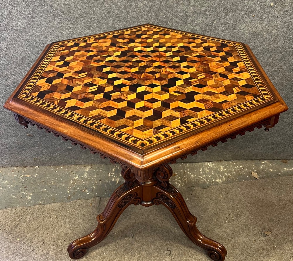 A 19th-century hexagonal specimen wood table featuring a geometric optical illusion parquetry top set on a carved central pedestal base.