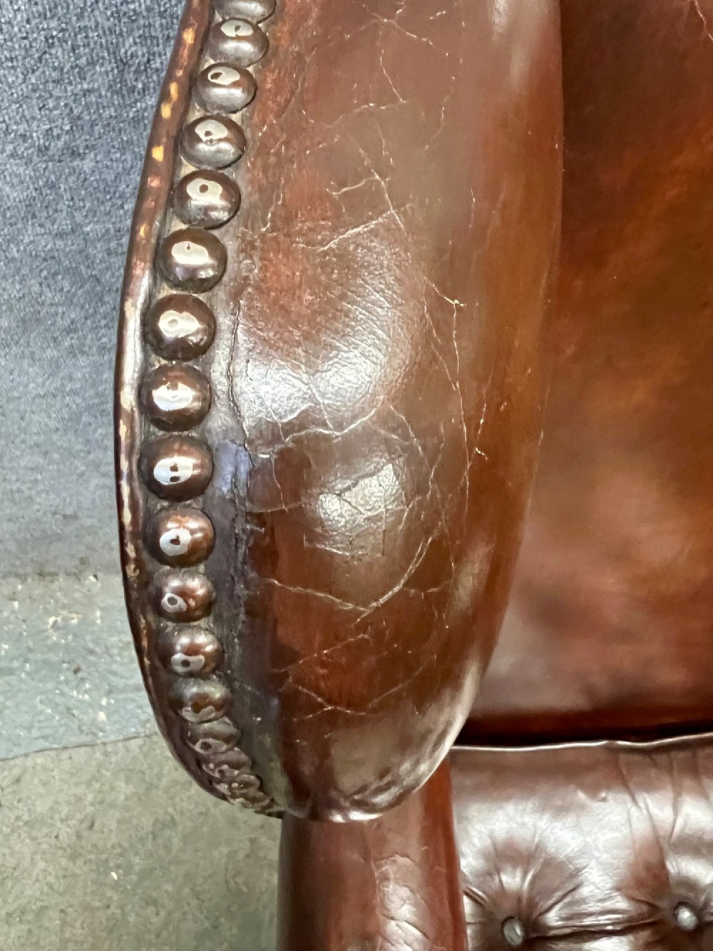 A Georgian style warm brown leather wingback armchair featuring a button-tufted seat cushion, brass stud trim, and dark timber legs. View III