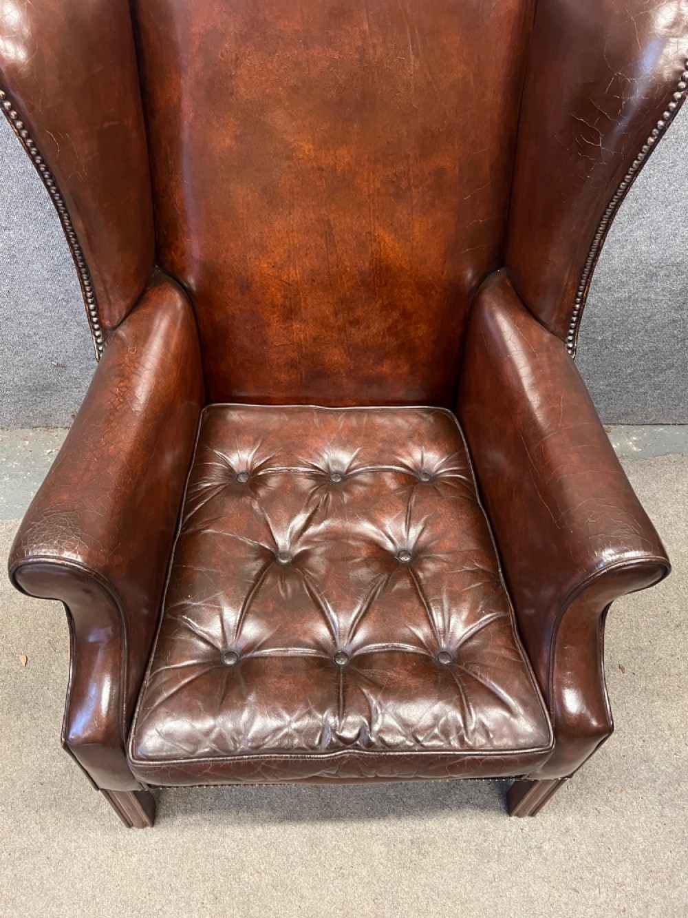 A Georgian style warm brown leather wingback armchair featuring a button-tufted seat cushion, brass stud trim, and dark timber legs. View VIII