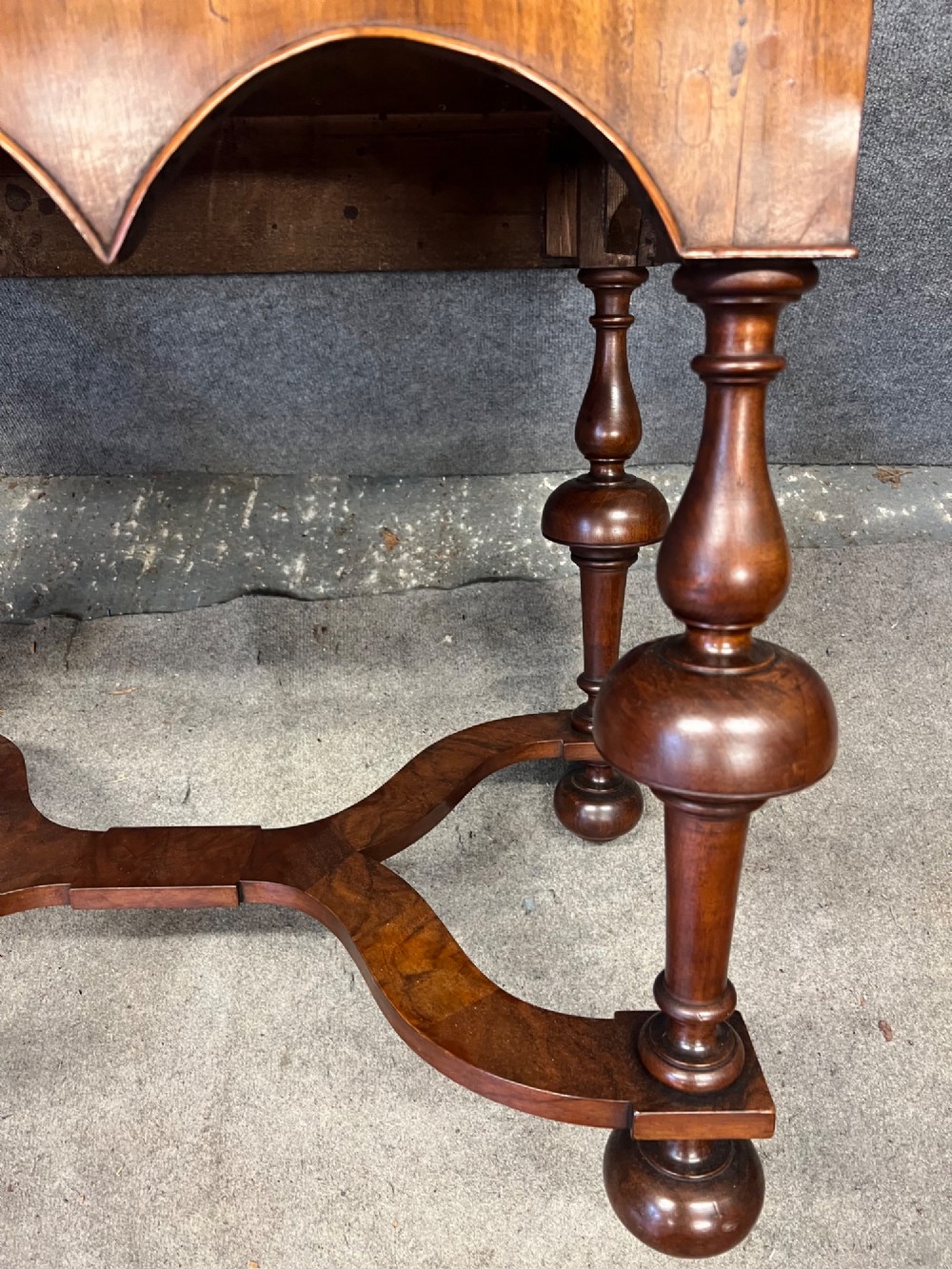 A William and Mary style walnut lowboy table featuring a quartered figured veneer top, a single drawer with brass drop handles, a shaped apron, turned legs, and a serpentine stretcher. View IX