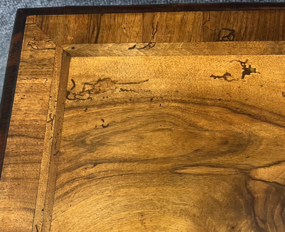 A William and Mary style walnut lowboy table featuring a quartered figured veneer top, a single drawer with brass drop handles, a shaped apron, turned legs, and a serpentine stretcher. View XII