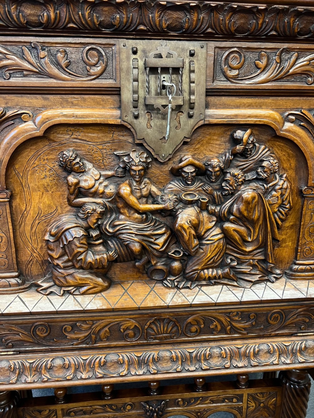 A carved Spanish vargueno cabinet in dark wood, featuring relief figures on the drop-front flap, decorative brass hardware, and a turned trestle stand. View III