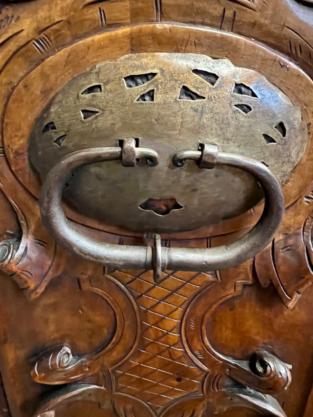 A carved Spanish vargueno cabinet in dark wood, featuring relief figures on the drop-front flap, decorative brass hardware, and a turned trestle stand. View VI