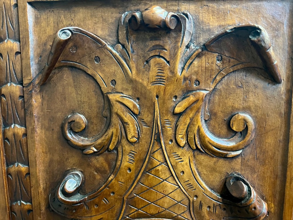 A carved Spanish vargueno cabinet in dark wood, featuring relief figures on the drop-front flap, decorative brass hardware, and a turned trestle stand. View VII