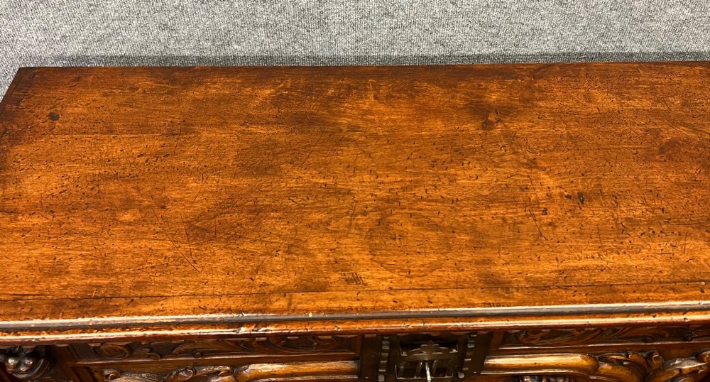 A carved Spanish vargueno cabinet in dark wood, featuring relief figures on the drop-front flap, decorative brass hardware, and a turned trestle stand. View VIII