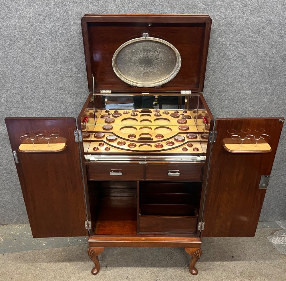 An open Art Deco walnut cocktail cabinet displaying a fitted mirrored interior with glassware, a silver-plated tray, and carved cabriole legs. View II