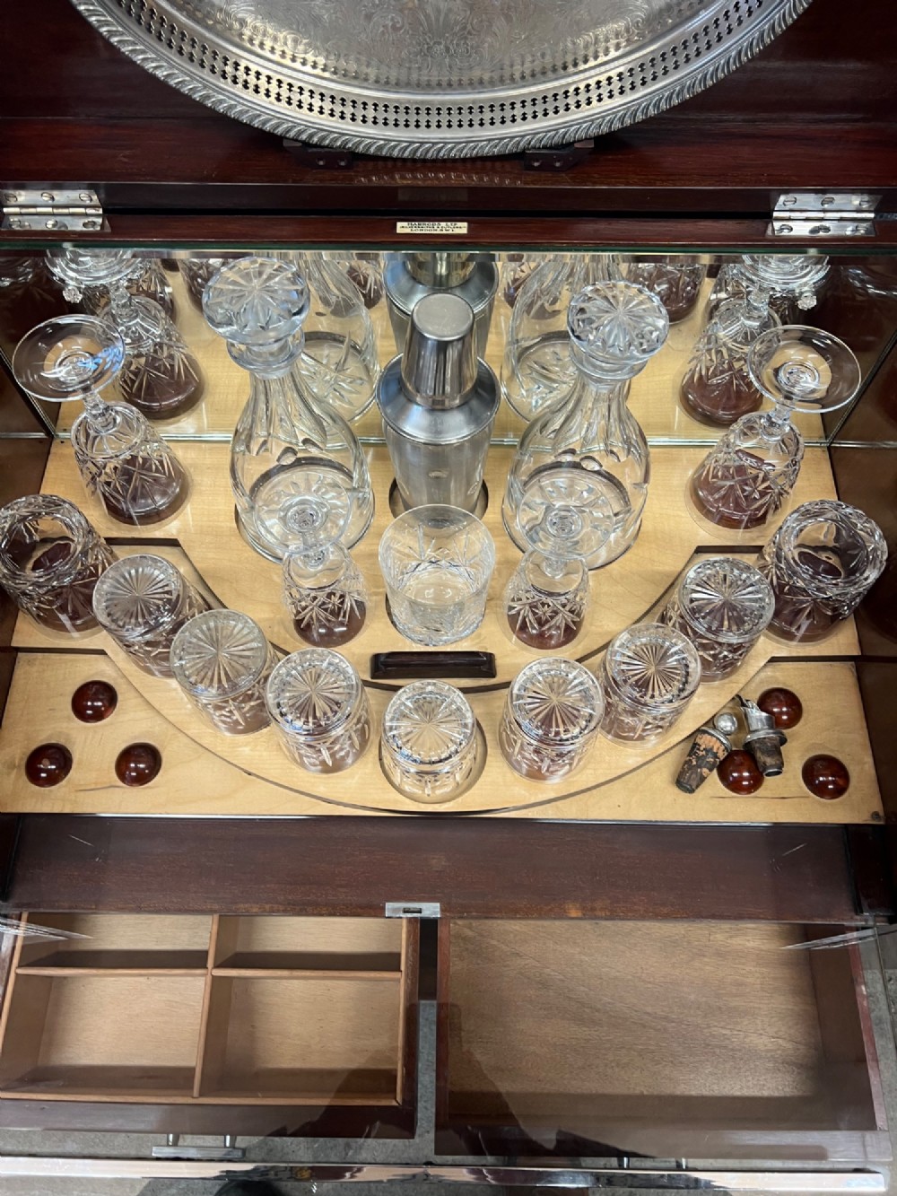 An open Art Deco walnut cocktail cabinet displaying a fitted mirrored interior with glassware, a silver-plated tray, and carved cabriole legs. View IV