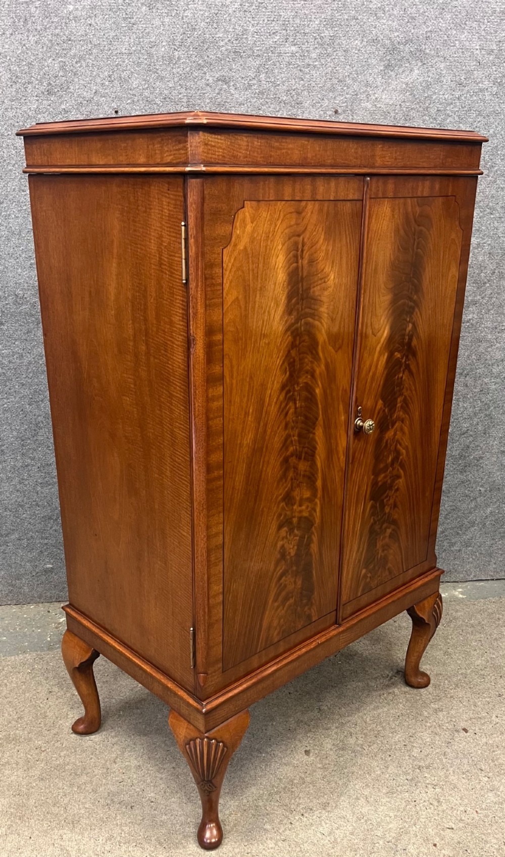 An open Art Deco walnut cocktail cabinet displaying a fitted mirrored interior with glassware, a silver-plated tray, and carved cabriole legs. View V