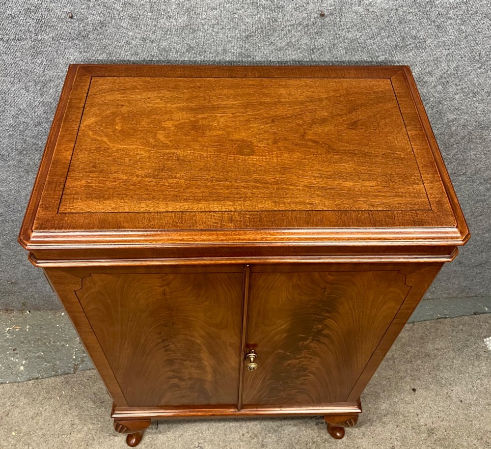 An open Art Deco walnut cocktail cabinet displaying a fitted mirrored interior with glassware, a silver-plated tray, and carved cabriole legs. View VII