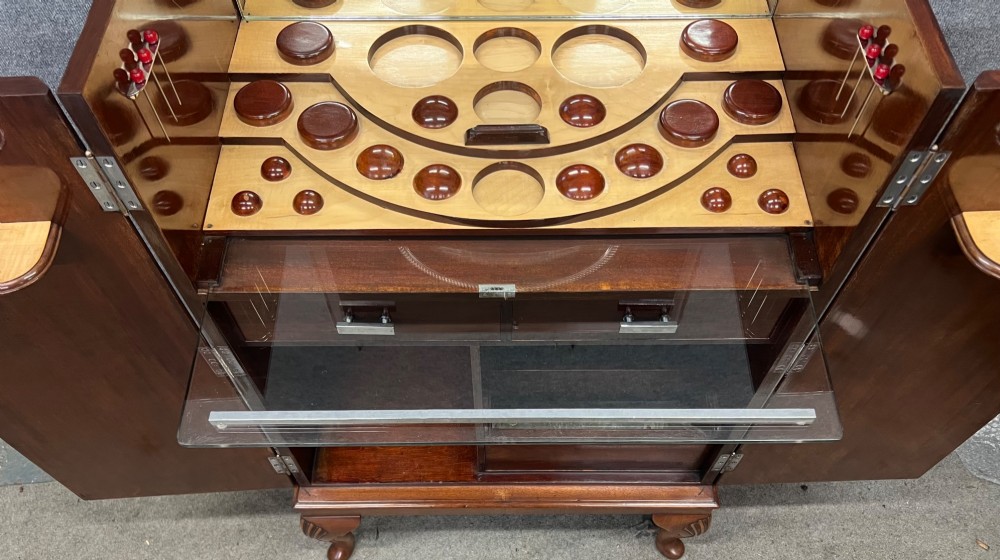 An open Art Deco walnut cocktail cabinet displaying a fitted mirrored interior with glassware, a silver-plated tray, and carved cabriole legs. View VIII