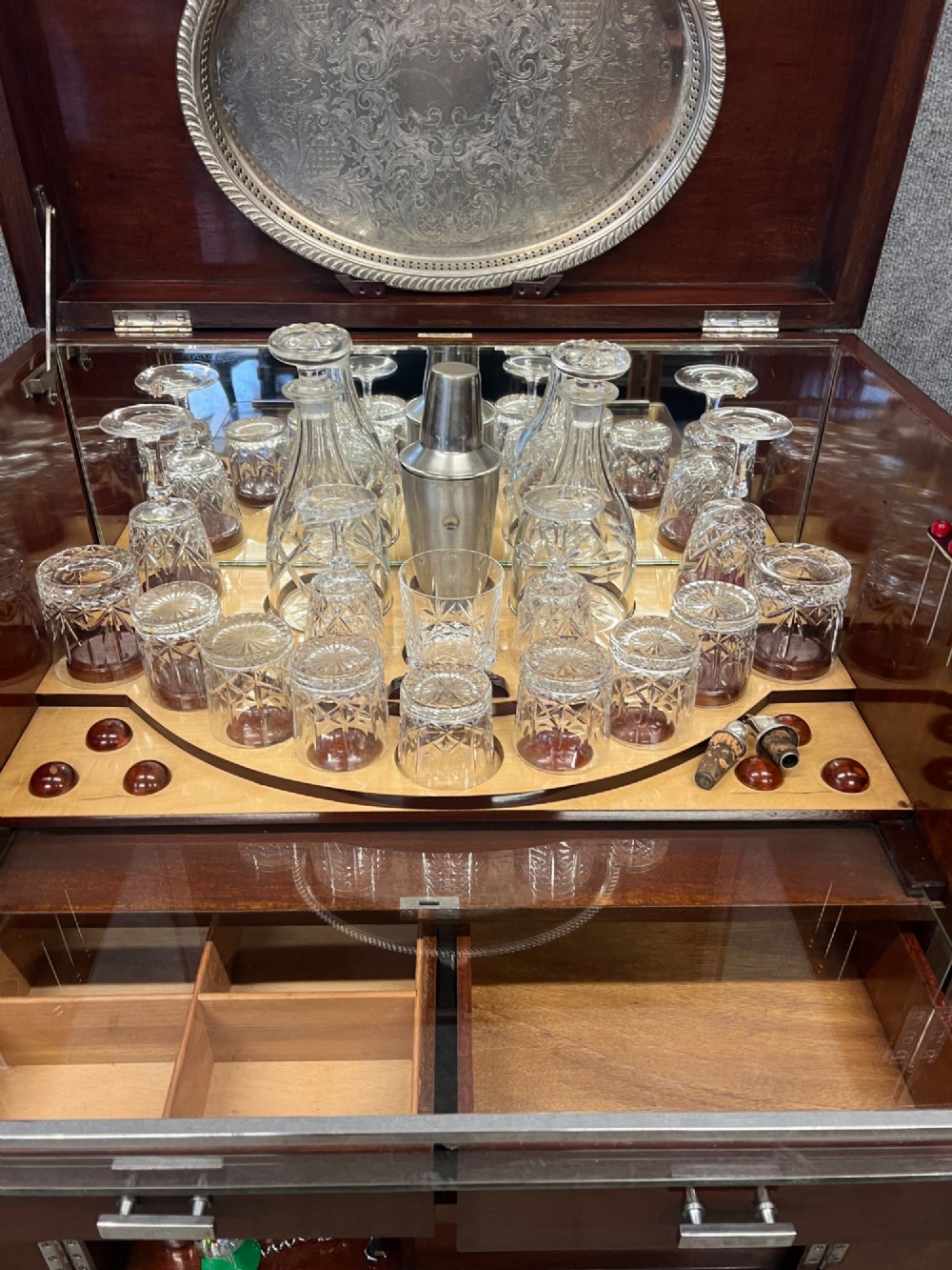 An open Art Deco walnut cocktail cabinet displaying a fitted mirrored interior with glassware, a silver-plated tray, and carved cabriole legs. View IX
