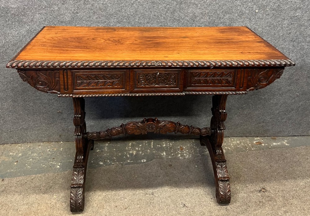 An Anglo-Indian carved hardwood centre table featuring a polished rectangular top, rope-twist carved borders, relief-carved frieze drawers, and detailed trestle legs.
