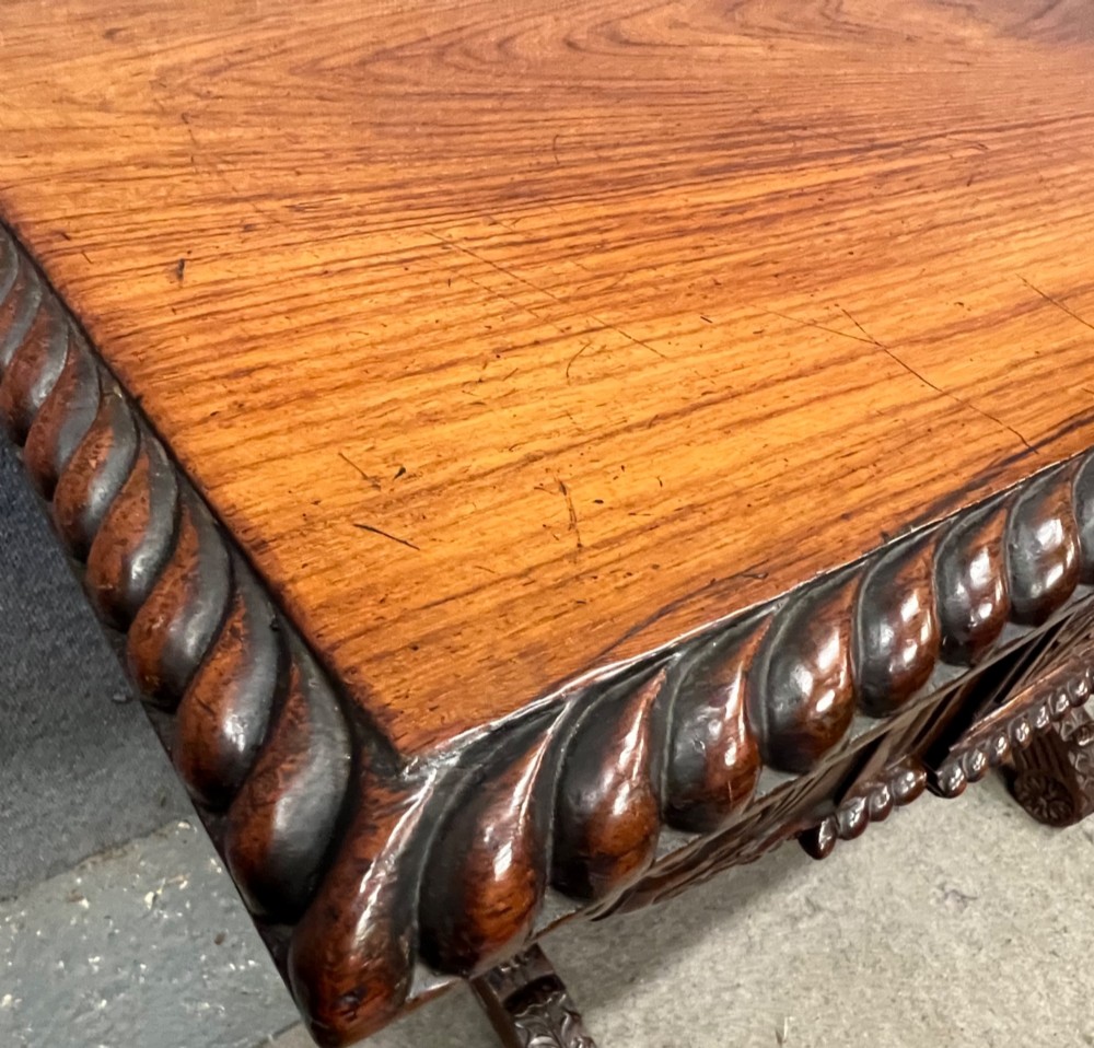An Anglo-Indian carved hardwood centre table featuring a polished rectangular top, rope-twist carved borders, relief-carved frieze drawers, and detailed trestle legs. View II