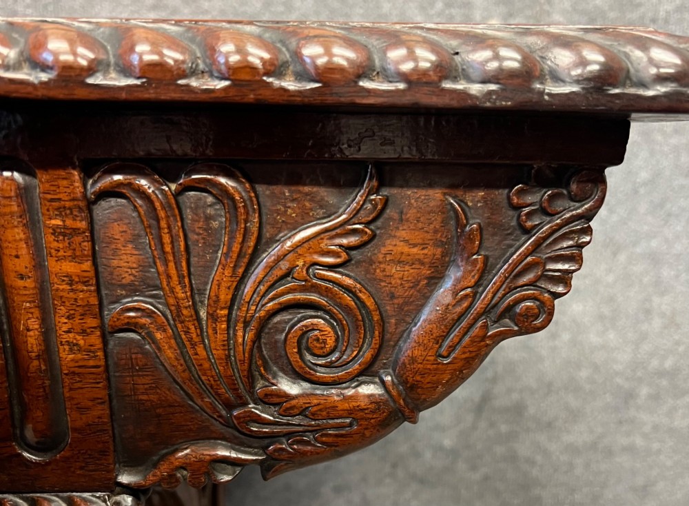 An Anglo-Indian carved hardwood centre table featuring a polished rectangular top, rope-twist carved borders, relief-carved frieze drawers, and detailed trestle legs. View IX