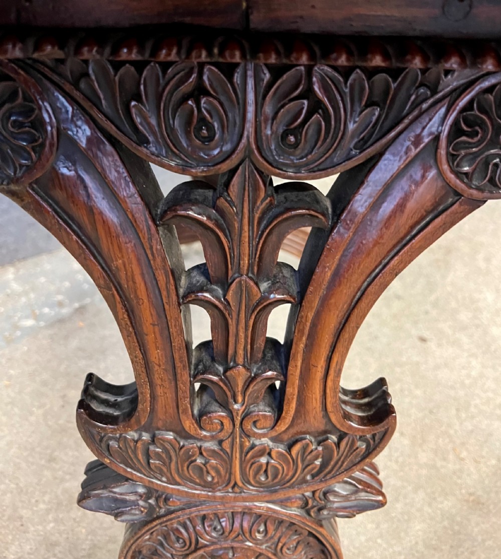 An Anglo-Indian carved hardwood centre table featuring a polished rectangular top, rope-twist carved borders, relief-carved frieze drawers, and detailed trestle legs. View X