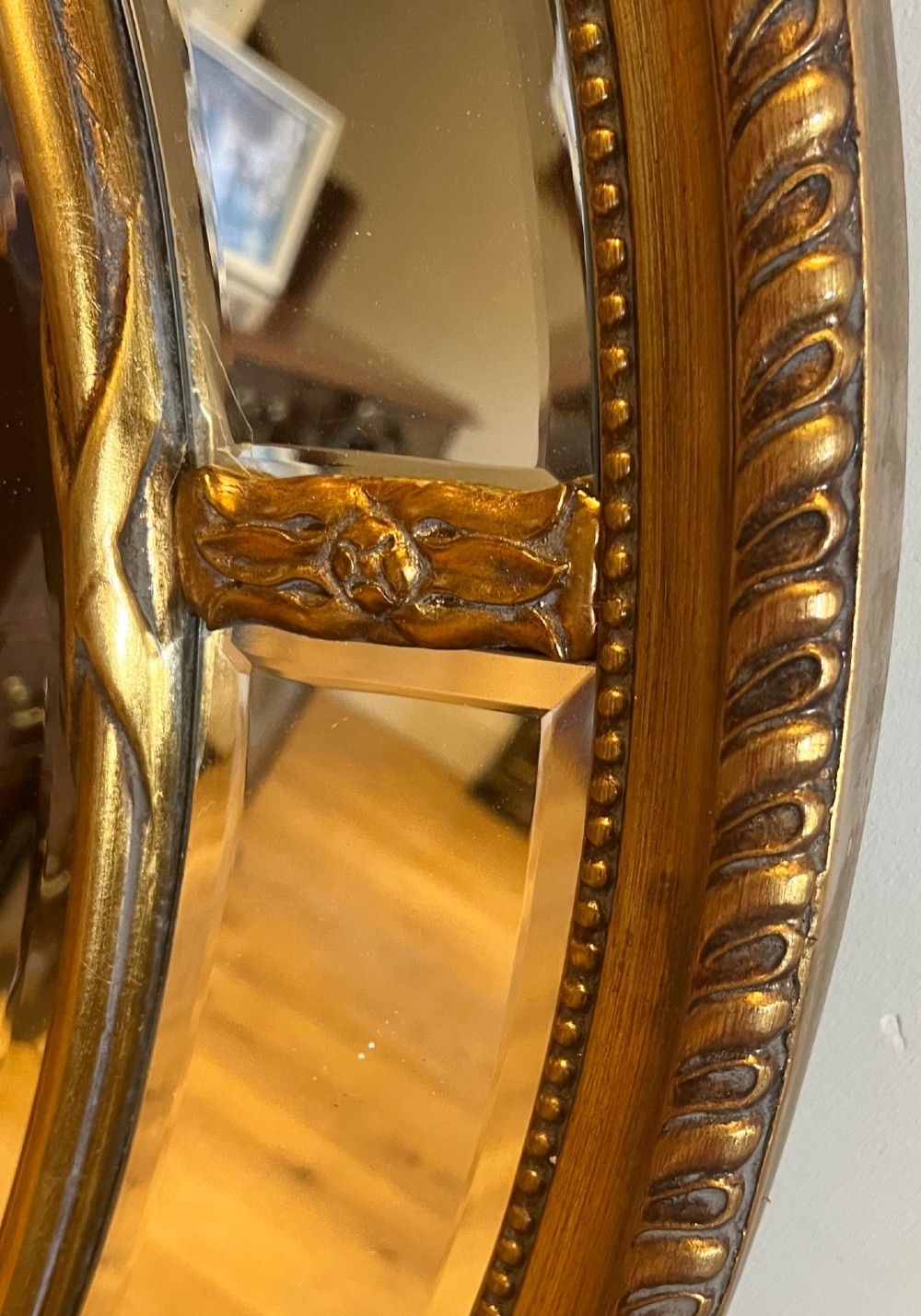 An oval gilded wall mirror featuring a bevelled central mirror surrounded by outer glass margin panels and a gadrooned rim. View IV