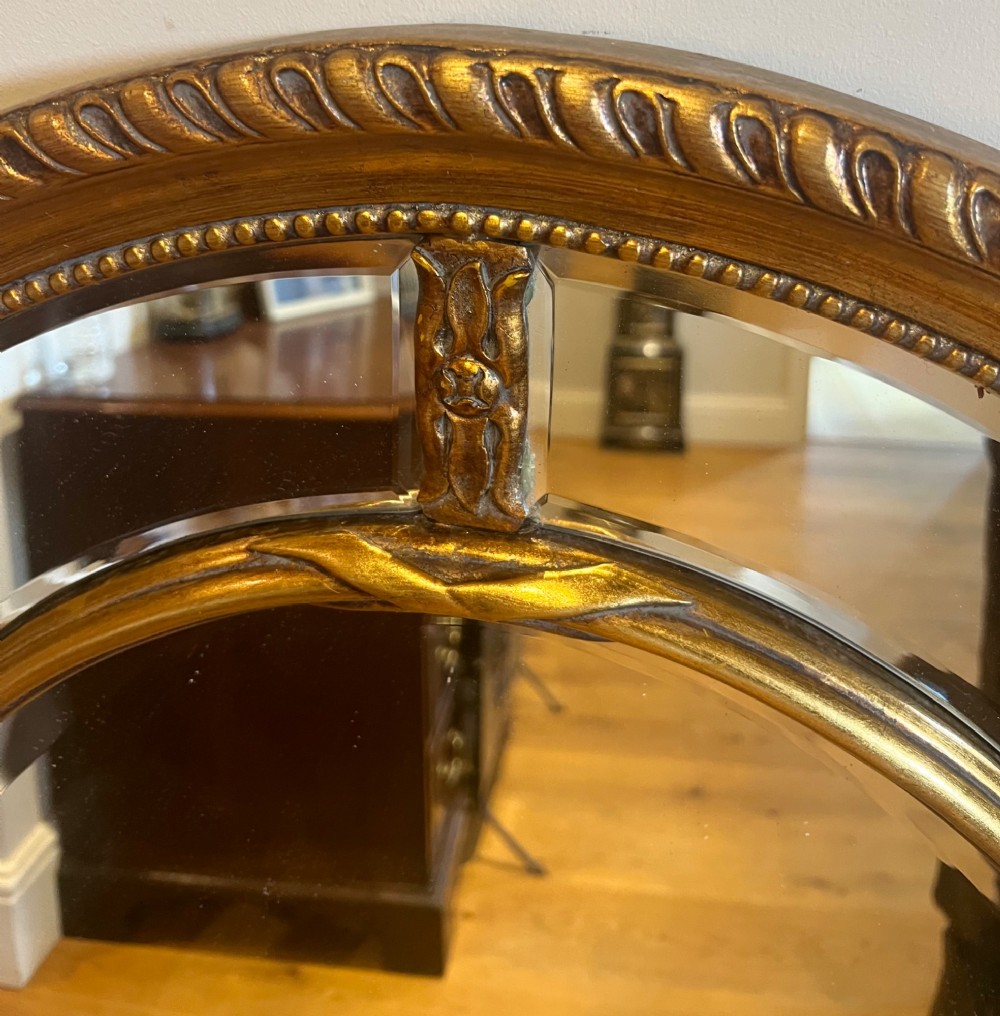 An oval gilded wall mirror featuring a bevelled central mirror surrounded by outer glass margin panels and a gadrooned rim. View V
