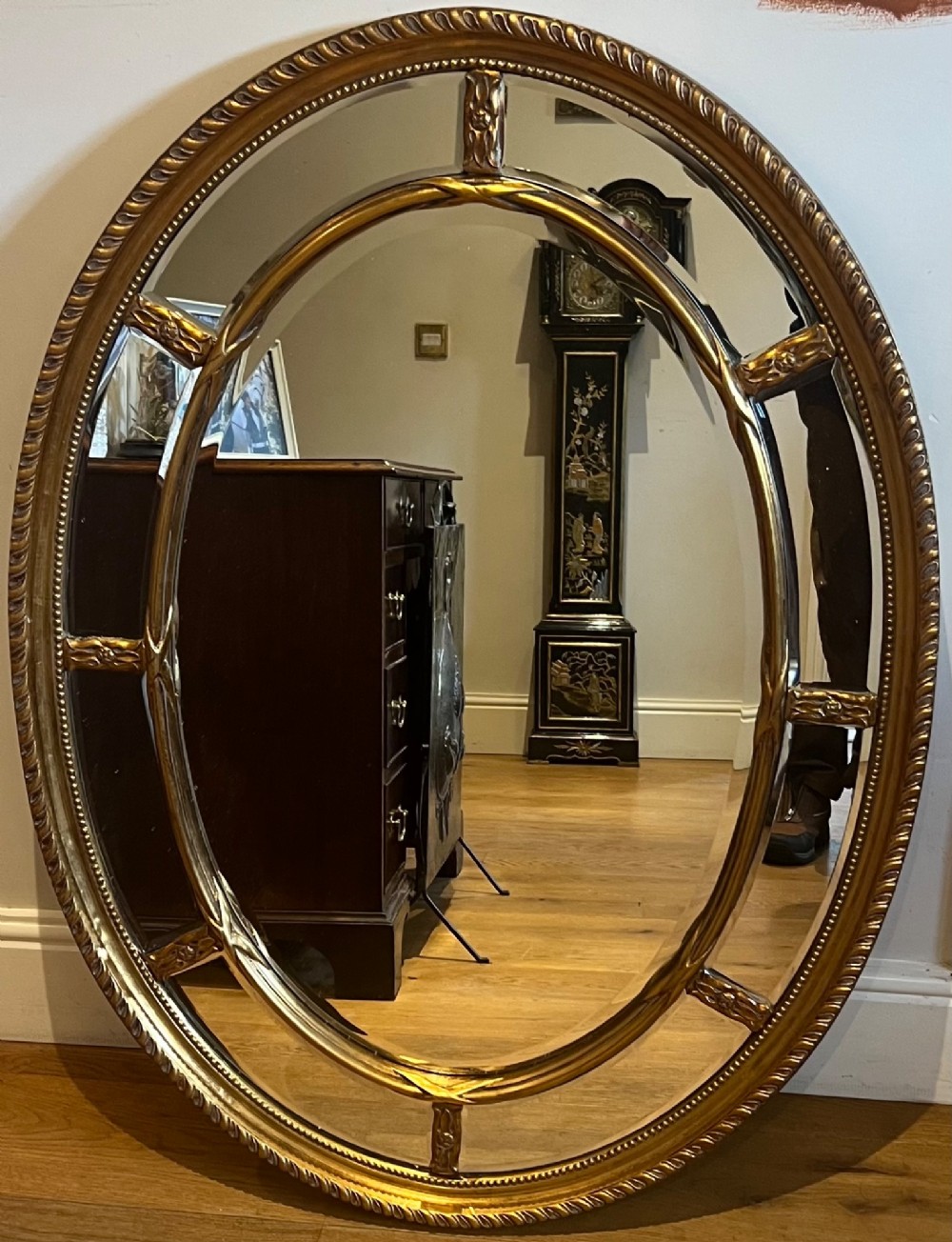 An oval gilded wall mirror featuring a bevelled central mirror surrounded by outer glass margin panels and a gadrooned rim. View VI