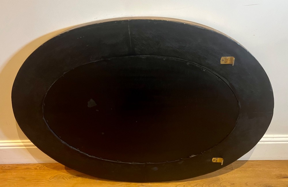 An oval gilded wall mirror featuring a bevelled central mirror surrounded by outer glass margin panels and a gadrooned rim. View IX
