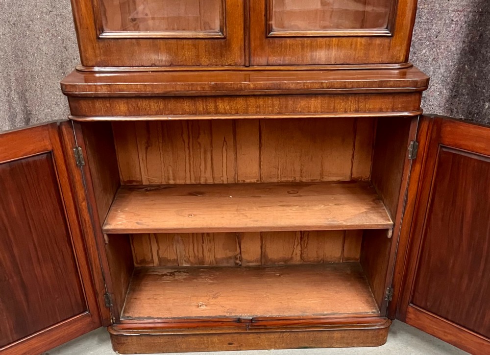 A two-door Victorian mahogany bookcase featuring an upper glazed cabinet with rounded corner panes and a lower enclosed wooden cupboard. View V