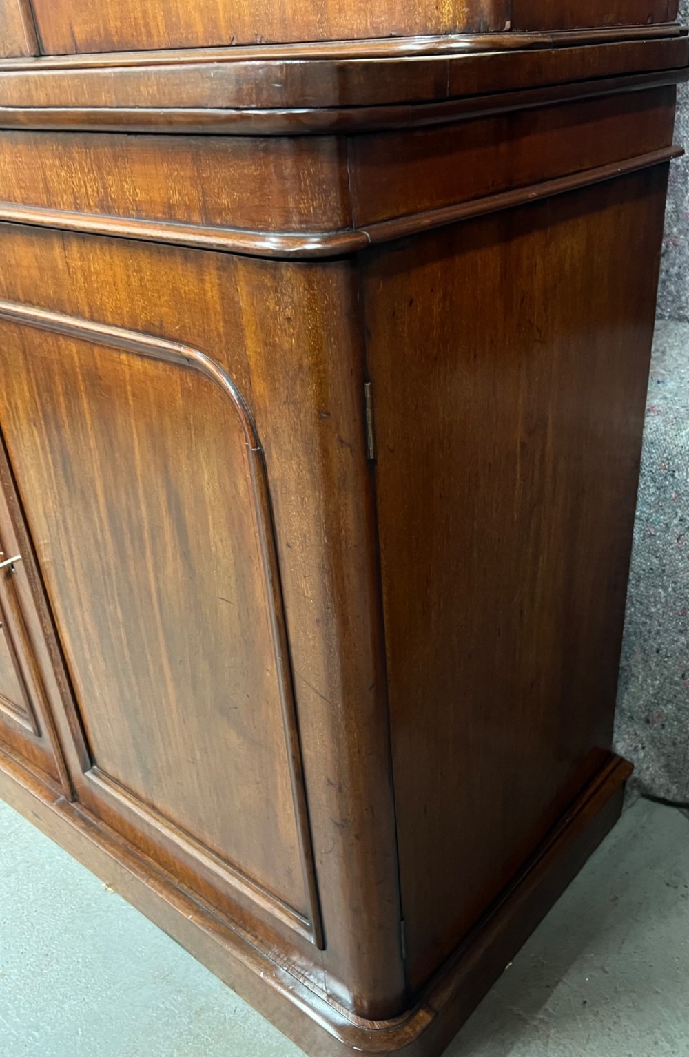 A two-door Victorian mahogany bookcase featuring an upper glazed cabinet with rounded corner panes and a lower enclosed wooden cupboard. View VII