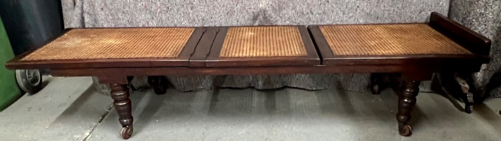 An antique mahogany campaign bed featuring three hinged folding sections with woven cane panelling and a dark timber frame. View III