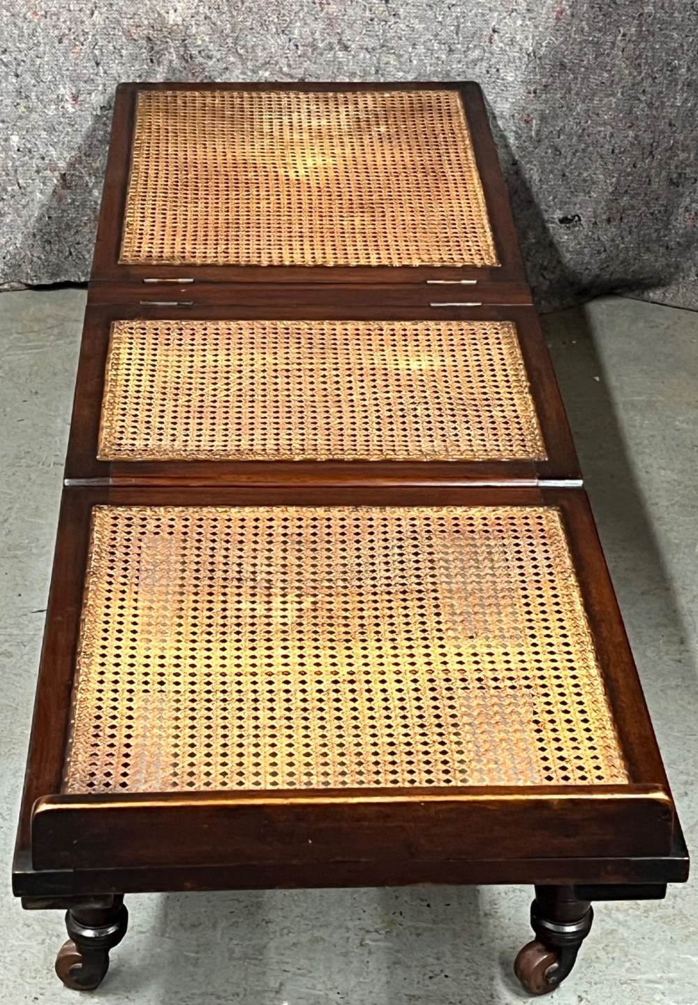 An antique mahogany campaign bed featuring three hinged folding sections with woven cane panelling and a dark timber frame. View VII