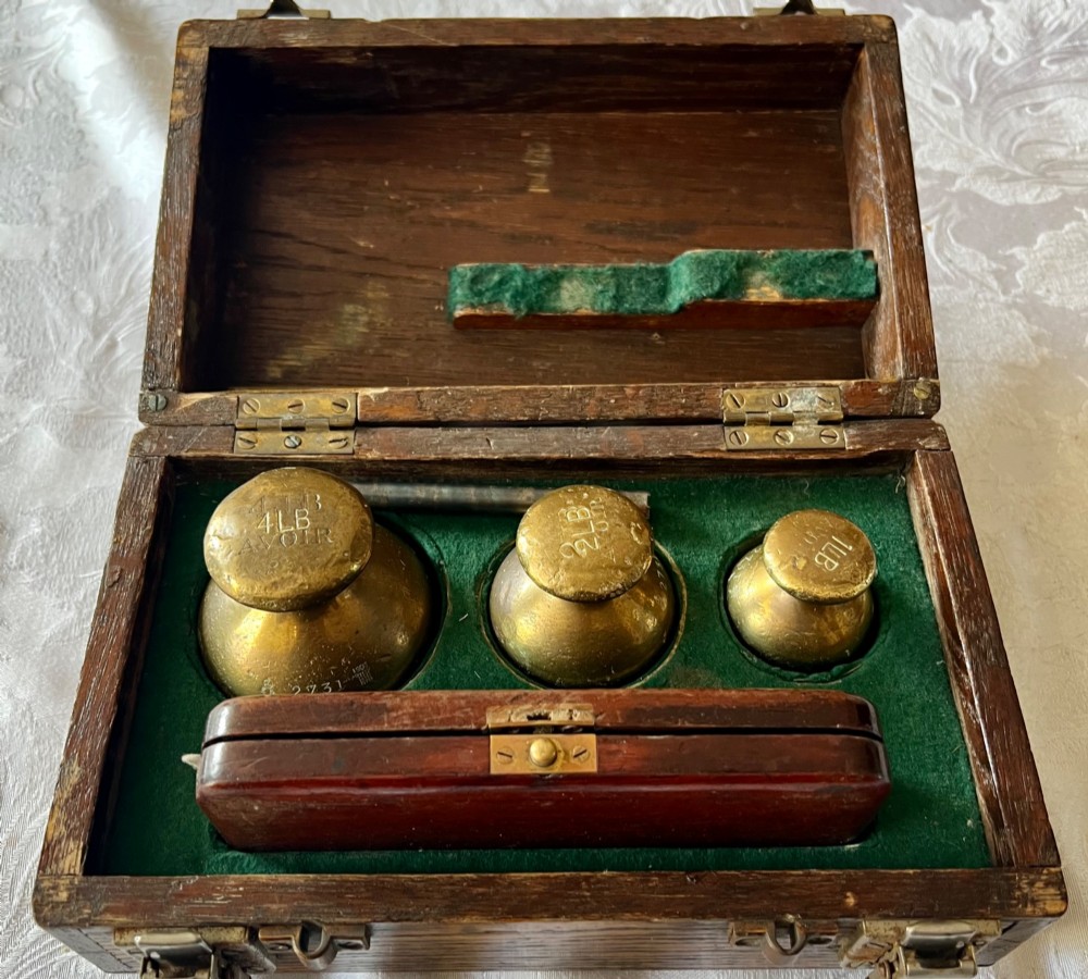 An open Edwardian wooden box lined with green baize, housing stamped brass imperial weights.