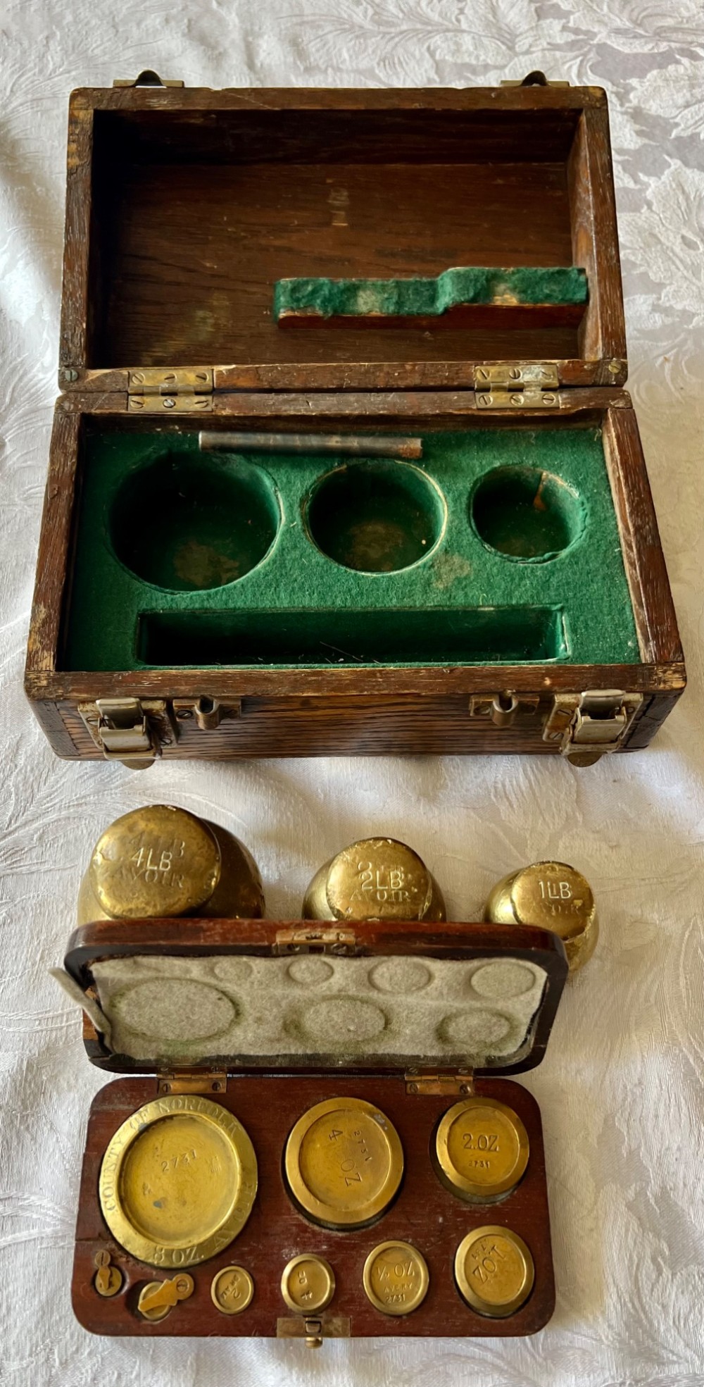 An open Edwardian wooden box lined with green baize, housing stamped brass imperial weights. View II