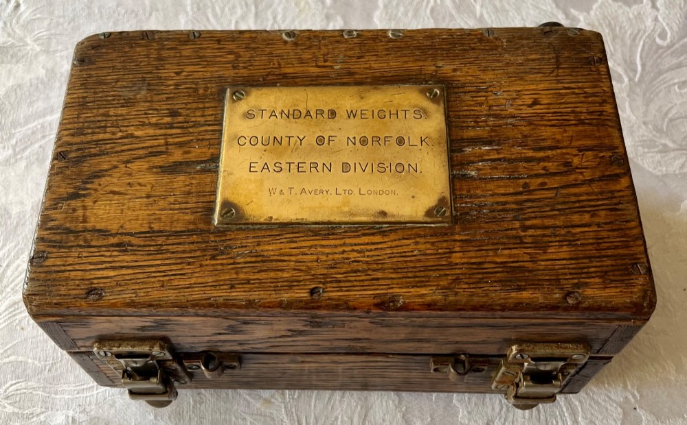 An open Edwardian wooden box lined with green baize, housing stamped brass imperial weights. View III