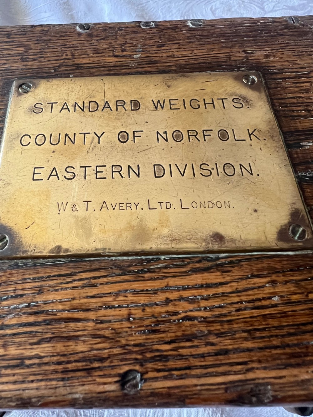 An open Edwardian wooden box lined with green baize, housing stamped brass imperial weights. View IV