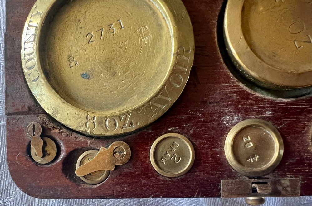An open Edwardian wooden box lined with green baize, housing stamped brass imperial weights. View VIII