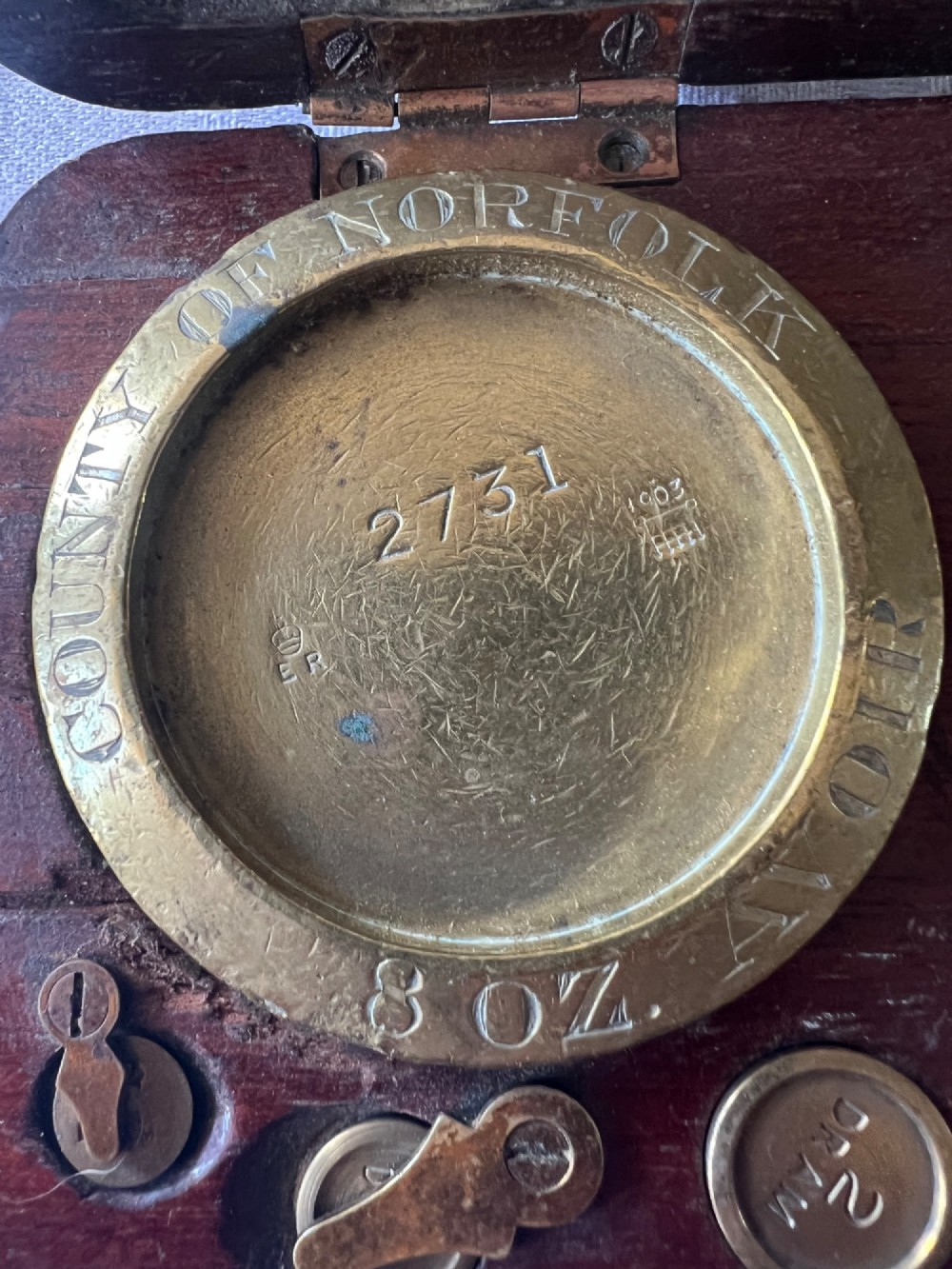 An open Edwardian wooden box lined with green baize, housing stamped brass imperial weights. View X