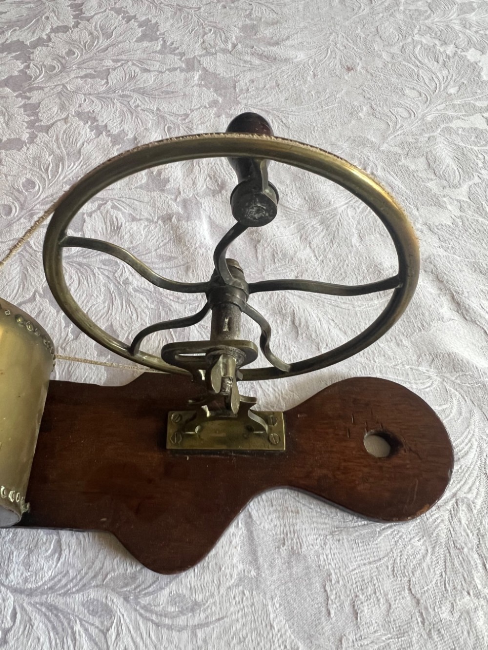 An antique mechanical rotary fireplace bellows featuring a mahogany wooden base, a brass spoked wheel with a hand crank, a driving band, and a brass casing leading to a tapered nozzle. View II