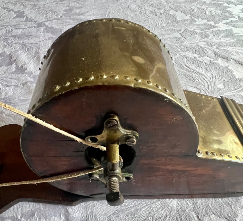 An antique mechanical rotary fireplace bellows featuring a mahogany wooden base, a brass spoked wheel with a hand crank, a driving band, and a brass casing leading to a tapered nozzle. View IV
