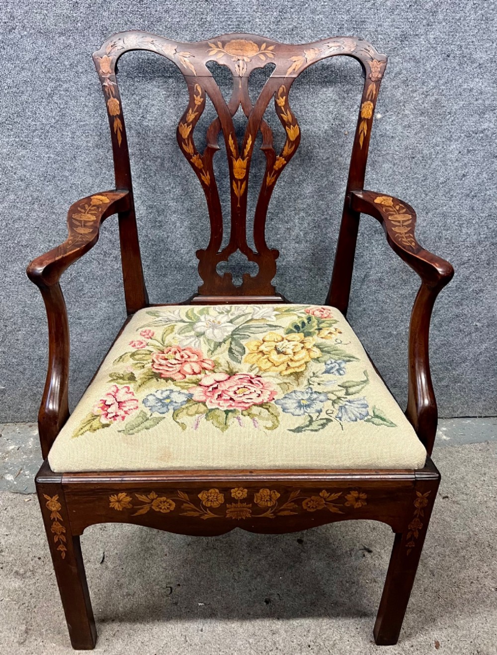 An antique mahogany armchair featuring floral marquetry wood inlays throughout the frame and splat, fitted with a floral needlepoint upholstered seat.