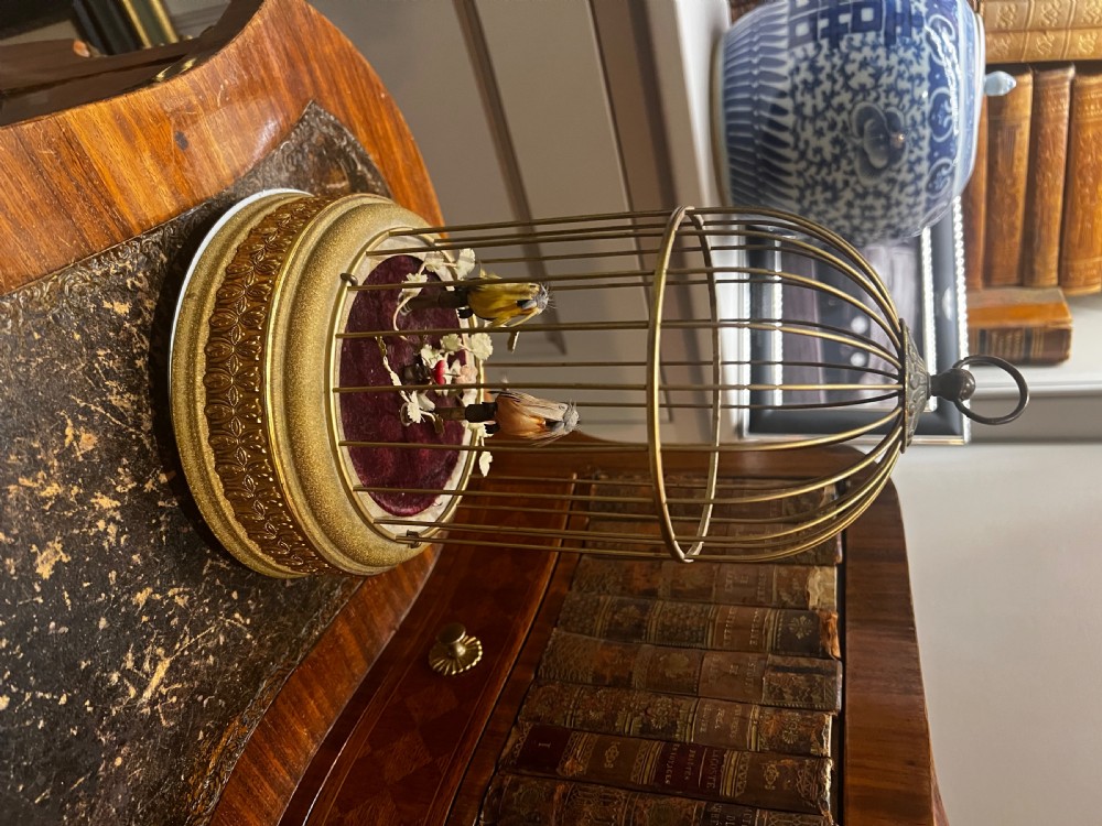 An antique brass caged singing bird automaton featuring two feathered mechanical birds on a velvet-lined base within an ornate dome-topped cage. View VI