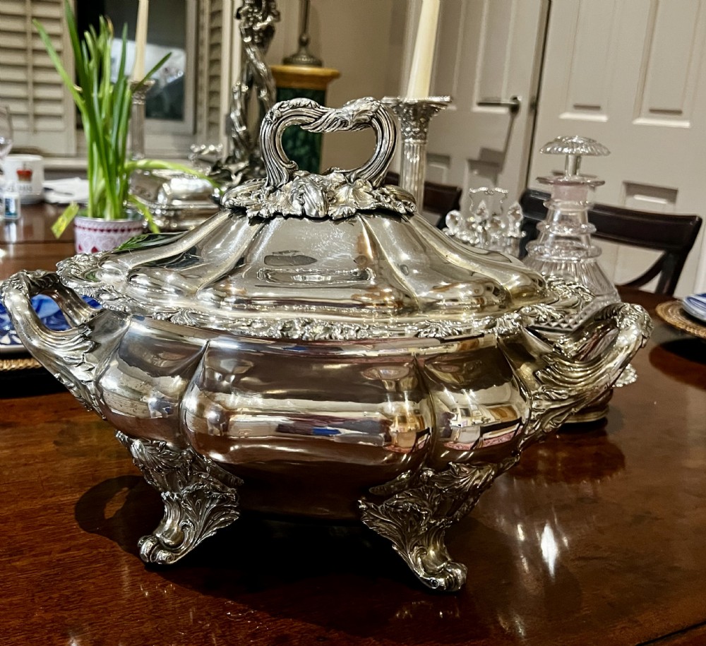 A Georgian silver plated soup tureen featuring a domed lobed lid, acanthus leaf handle, cast foliage feet, and twin side handles.